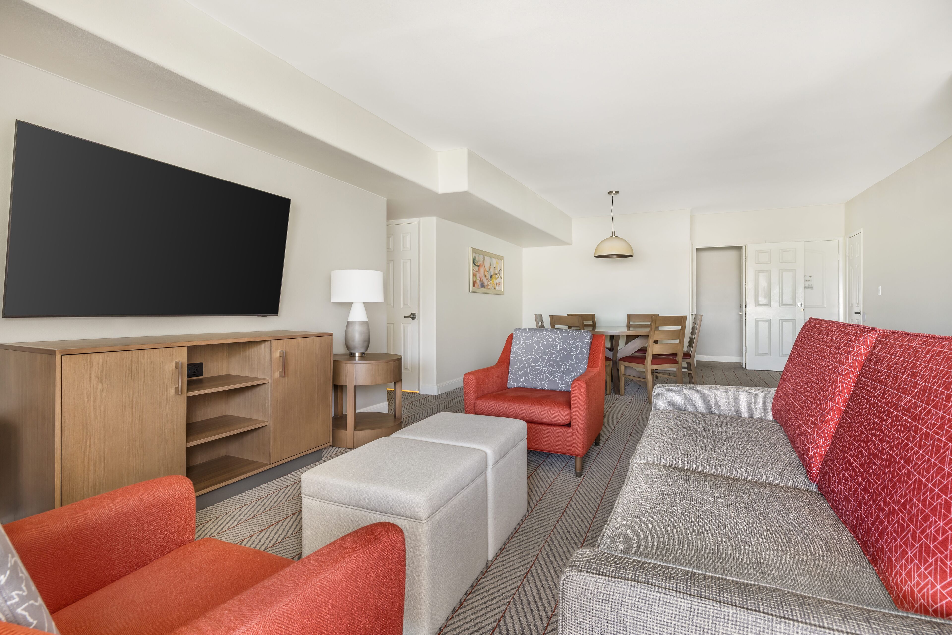 Ein modernes Wohnzimmer mit einem Flachbildfernseher, roten und grauen Sofas, einer Holzkommode und einem Essbereich mit Tisch und Stühlen.