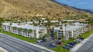 A multi-story hotel with a parking lot, surrounded by palm trees and mountains.