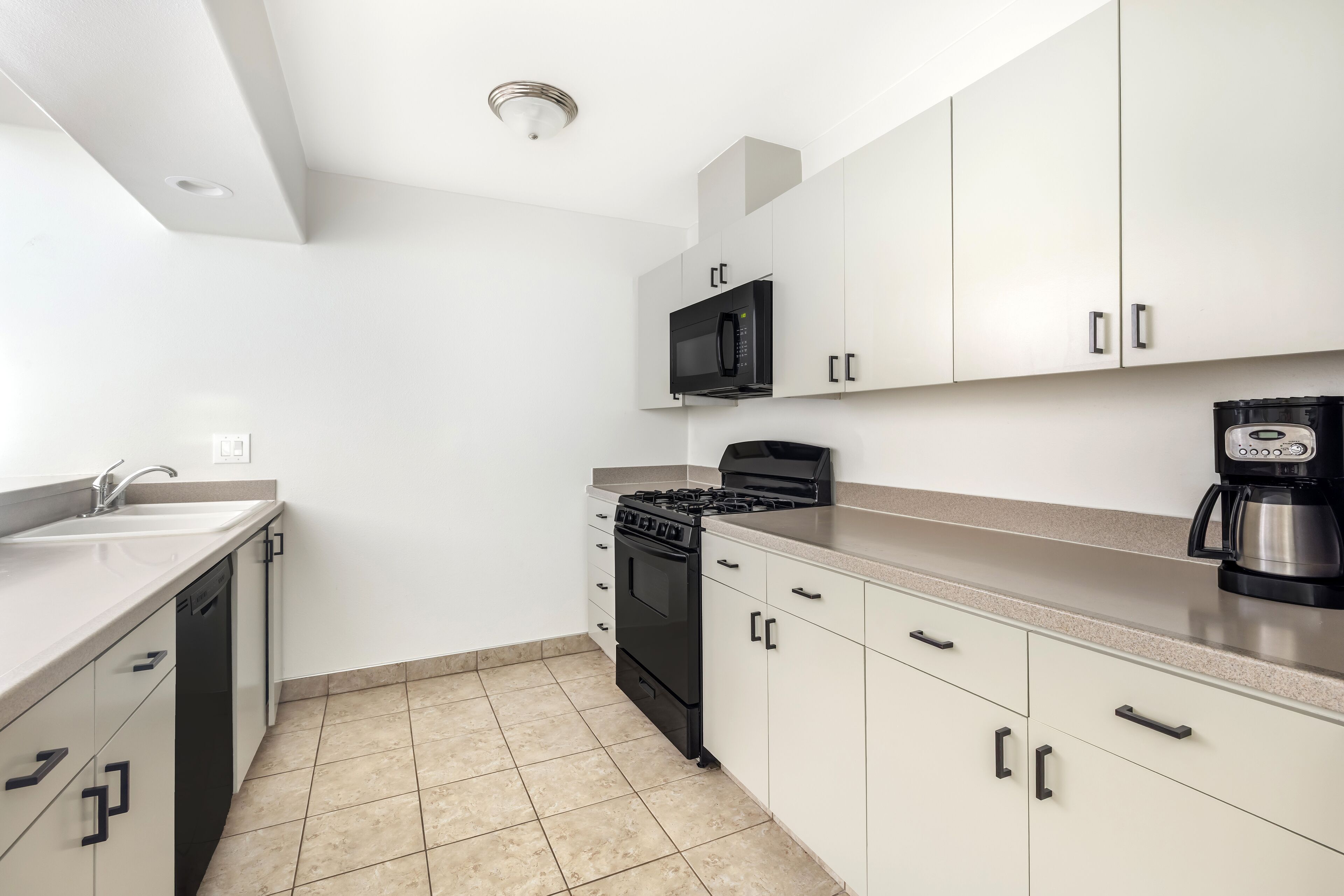 A modern kitchen with white cabinets, a black stove, a microwave, and a coffee maker.