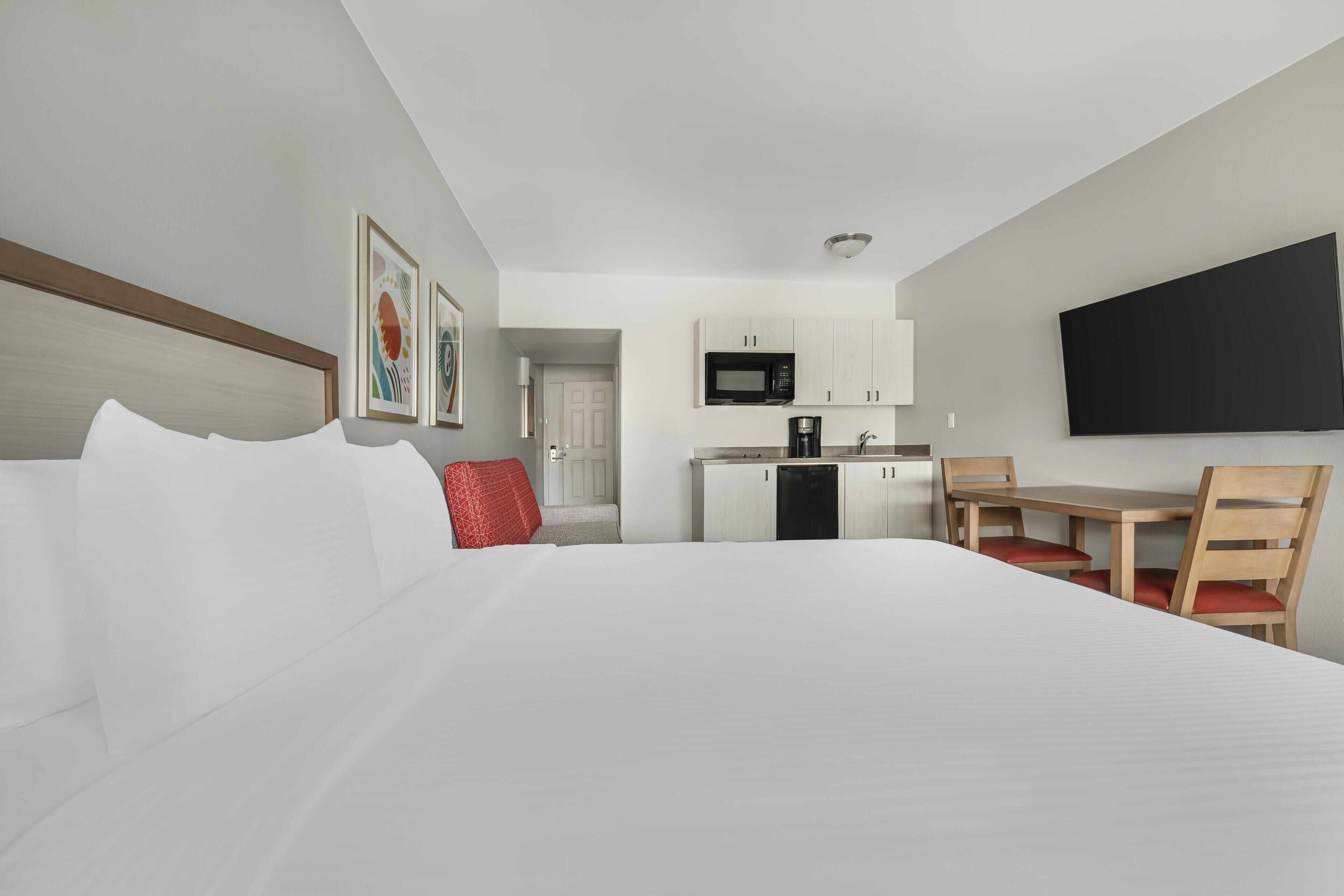 A hotel room with a bed, a desk, a chair, a microwave, and a TV.