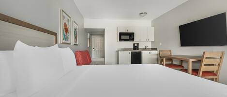 A hotel room with a bed, a desk, a chair, a microwave, and a TV.
