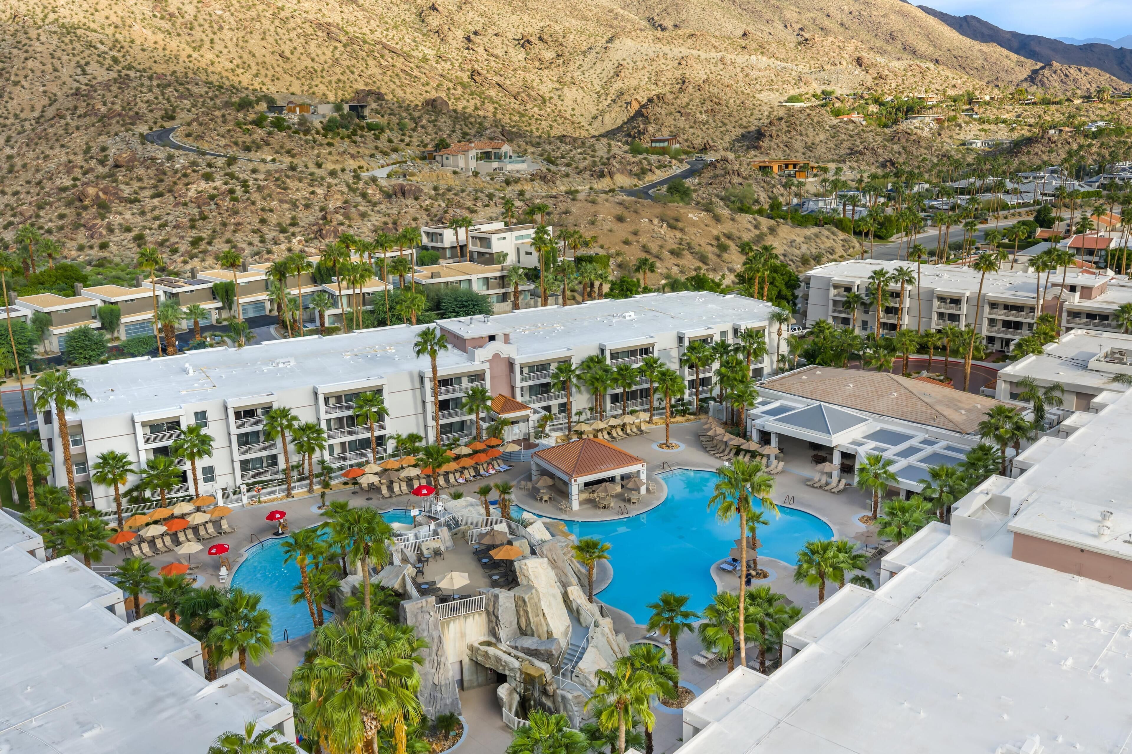 Un resort con piscina, palmeras y montañas al fondo.