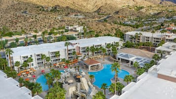 Un resort con piscina, palmeras y montañas al fondo.