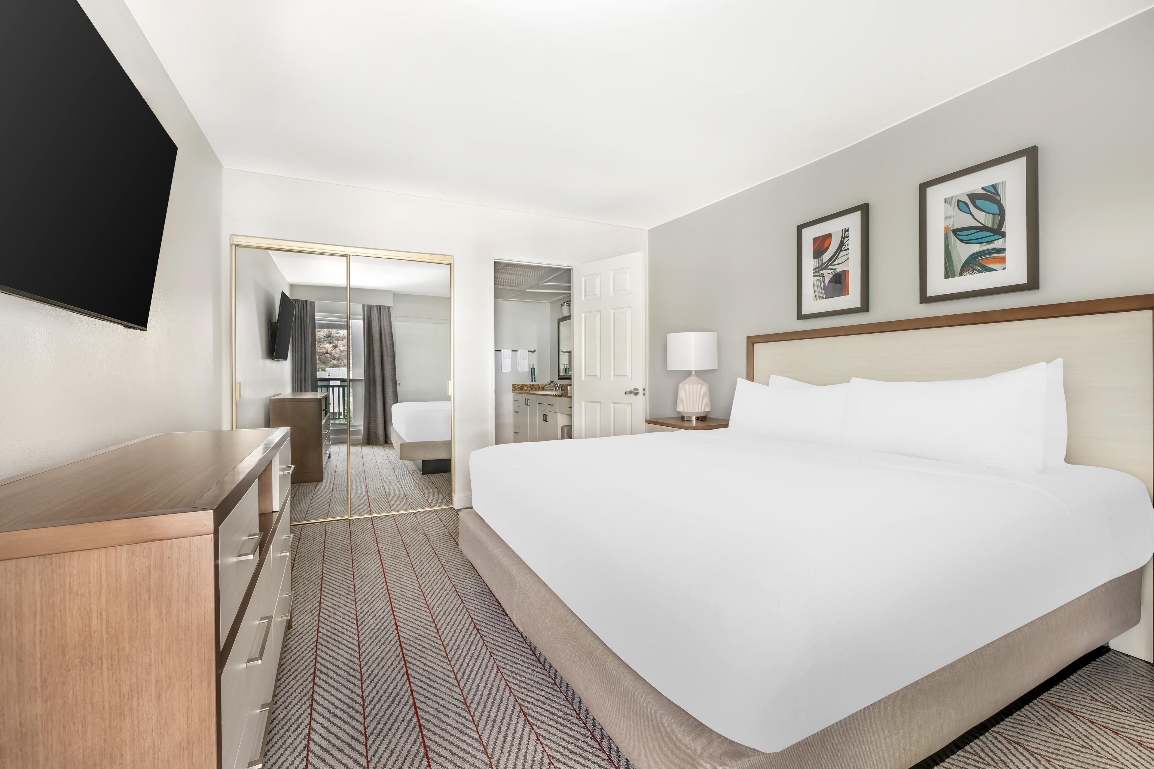 Une chambre d’hôtel avec un grand lit, un bureau, un miroir et des œuvres d’art accrochées au mur.