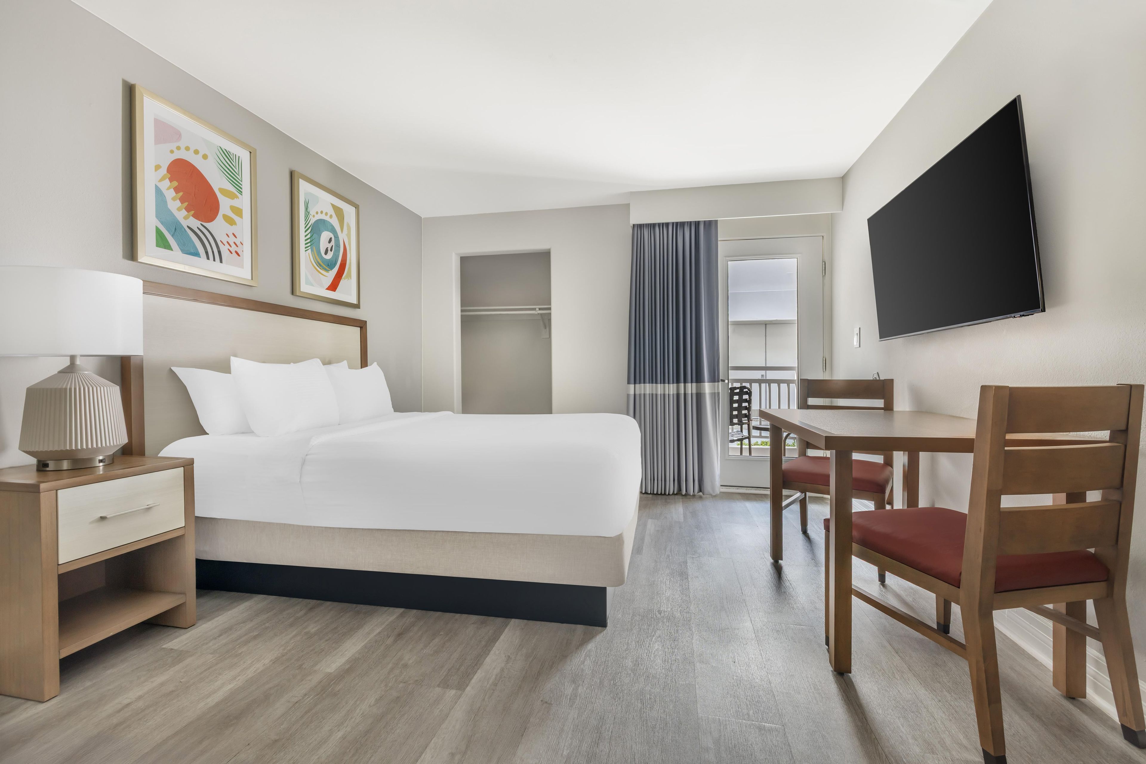 A hotel room with a bed, bedside table, lamp, chair, and a TV mounted on the wall.