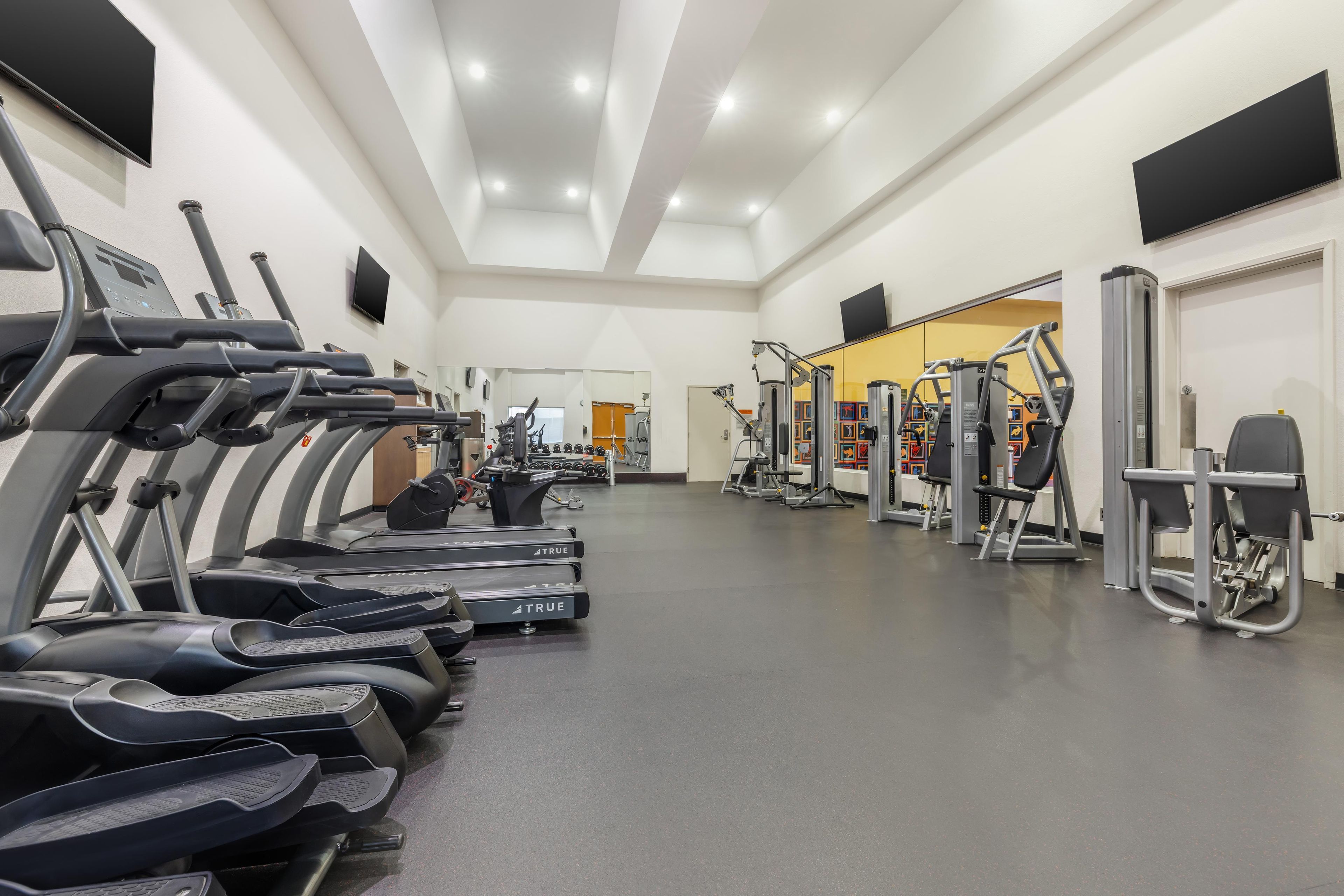 Uma academia com várias esteiras, aparelhos de musculação e um espelho grande.
