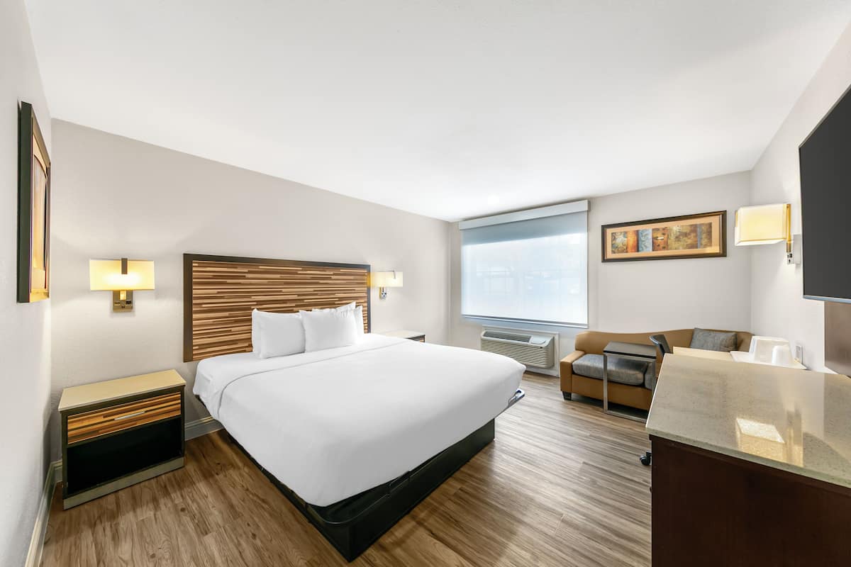 Hotellihuone, jossa on suuri sänky, puinen pääty, työpöytä, tuoli ja ikkuna, jossa on sälekaihtimet.
