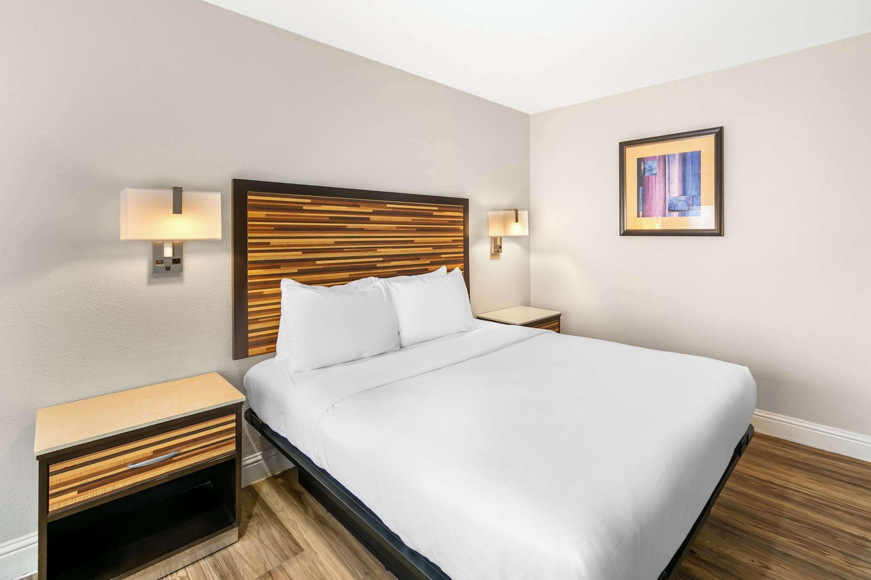 A neatly made bed with a wooden headboard, two bedside tables with lamps, and a framed picture on the wall.