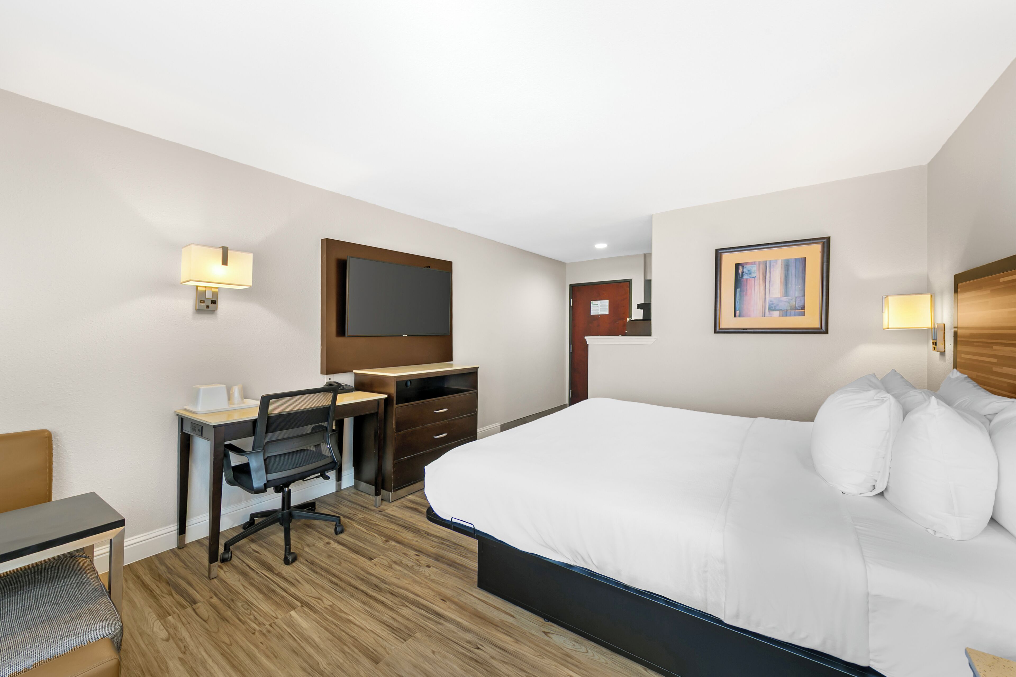 A hotel room with a bed, desk, chair, and a flat-screen TV.