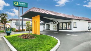 Ein Gebäude der Quality Inn & Suites by Choice Hotels mit überdachter Einfahrt, gepflegtem Rasen und blauem Himmel.