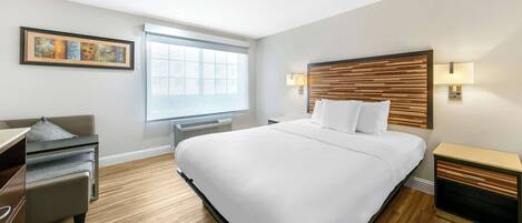 A modern hotel room with a large bed, a desk, a chair, and a window with blinds.