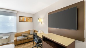Ein modernes Hotelzimmer mit einem Bett, einem Schreibtisch mit Stuhl, einer Couch, einem Flachbildfernseher, einer Wandleuchte und einem gerahmten Bild an der Wand.