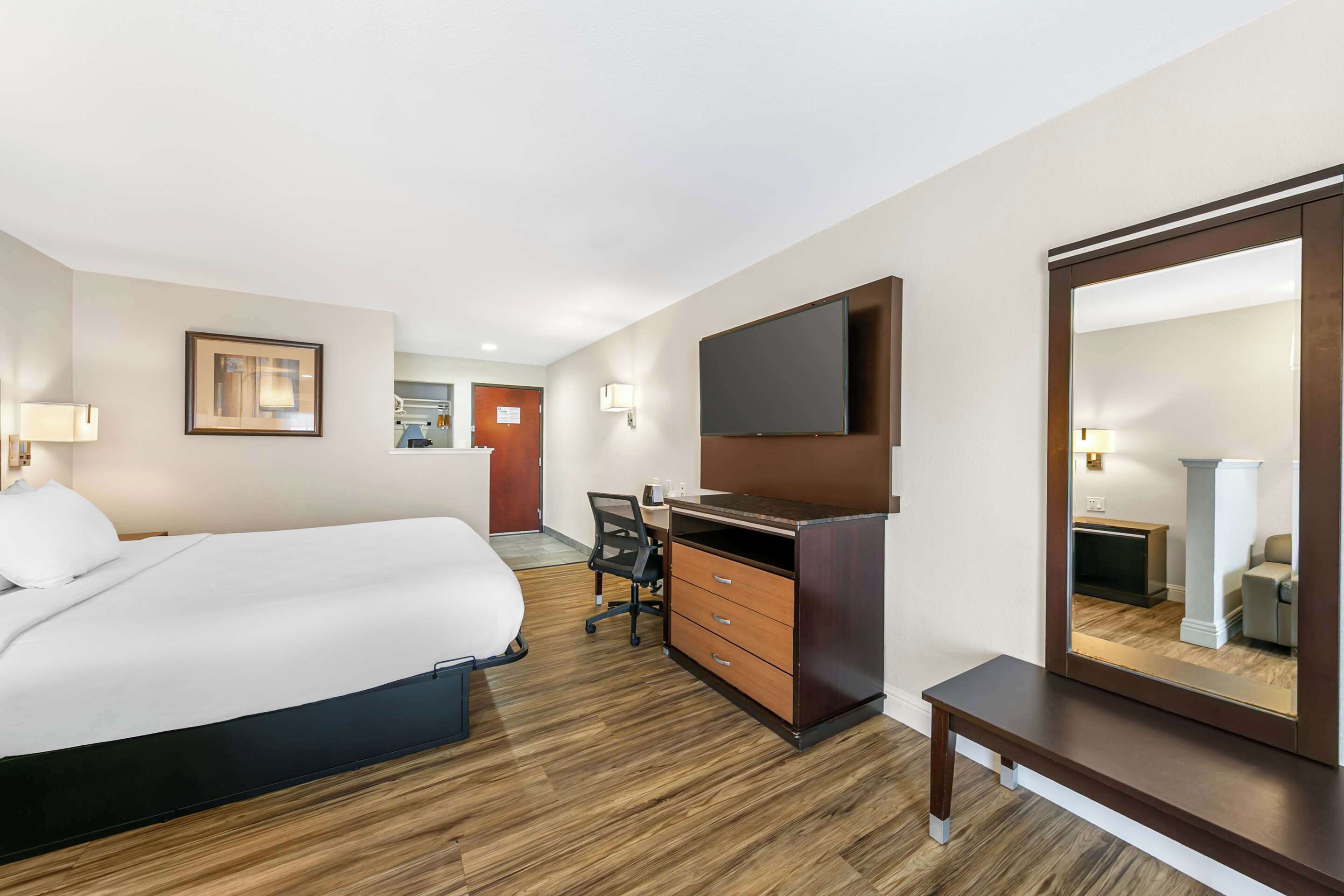 A hotel room with a bed, desk, chair, and a large mirror.