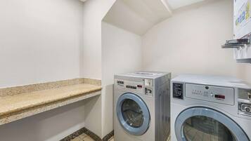 A laundry room with two front-loading washing machines, a countertop, and a wall-mounted dryer.