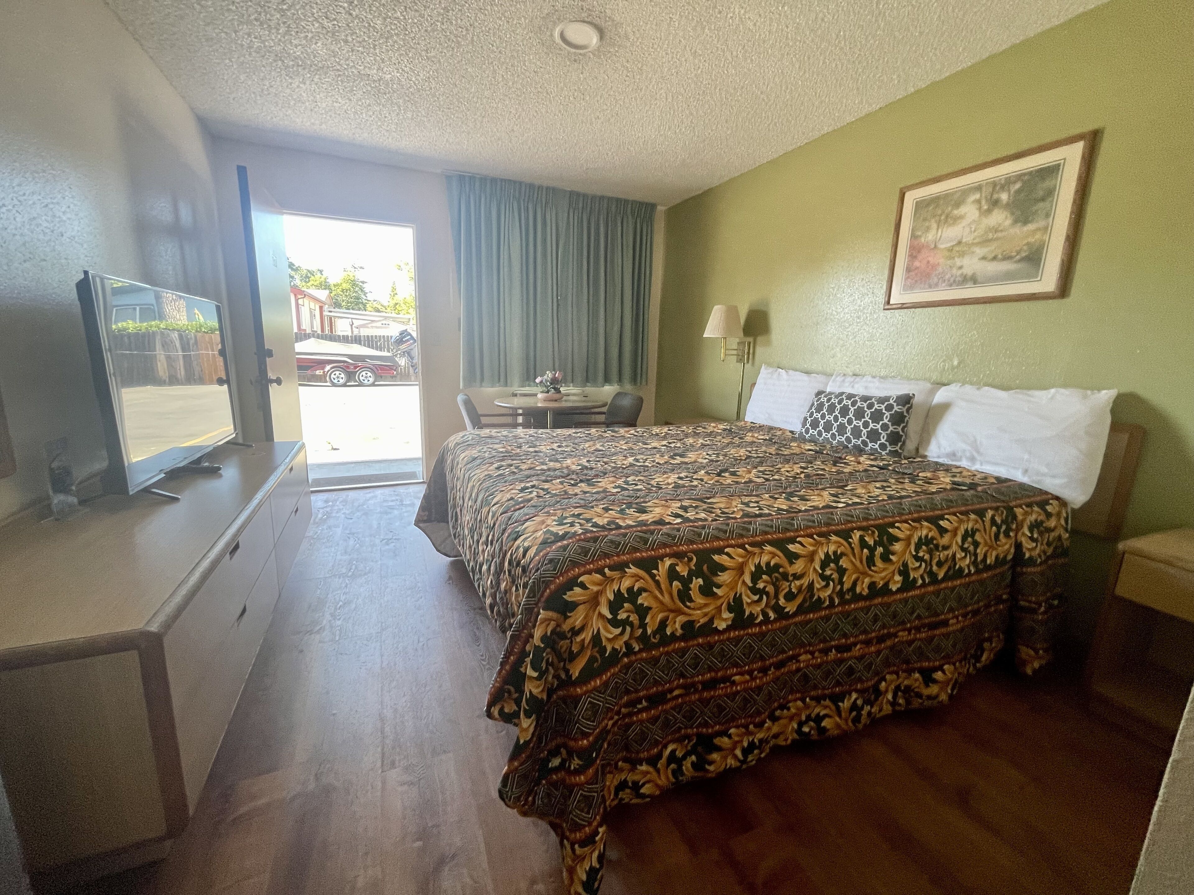 Una habitación de hotel con cama, escritorio, silla, lámpara y televisor.