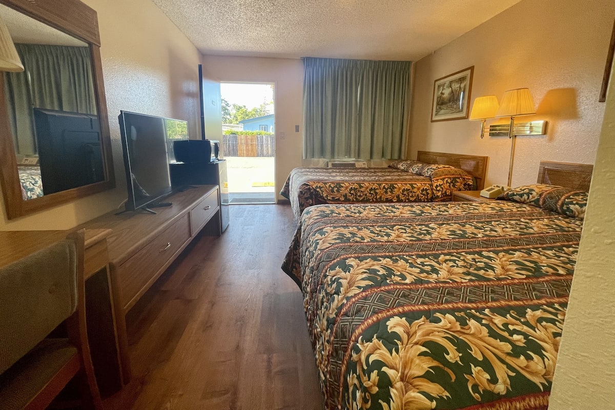 A hotel room with two beds, a television, a desk, and a window with curtains.