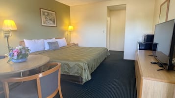 A hotel room with a bed, a desk with a chair, a television, and a framed picture on the wall.
