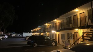 A motel with a parking lot, a black car parked in front, and a staircase leading to the entrance. - Regency Inn (Lakeport)