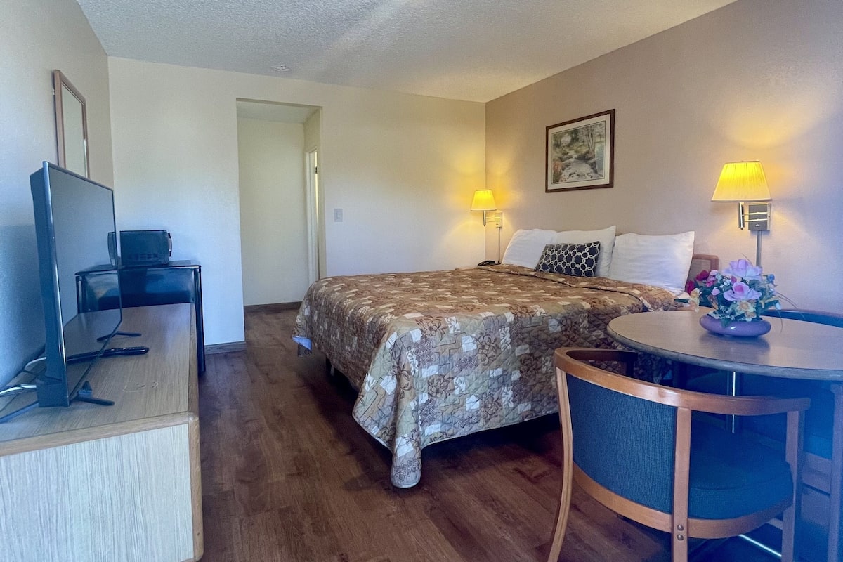 A hotel room with a bed, a desk with a computer, a chair, and two bedside lamps.