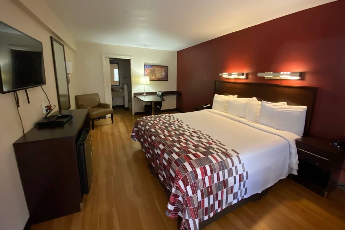 A hotel room with a large bed, a desk, a TV, and a small kitchenette.