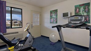 A hotel room with a treadmill, exercise bike, and a window with curtains. - California Inn & Suites Rancho Cordova - Sacramento (Rancho Cordova)