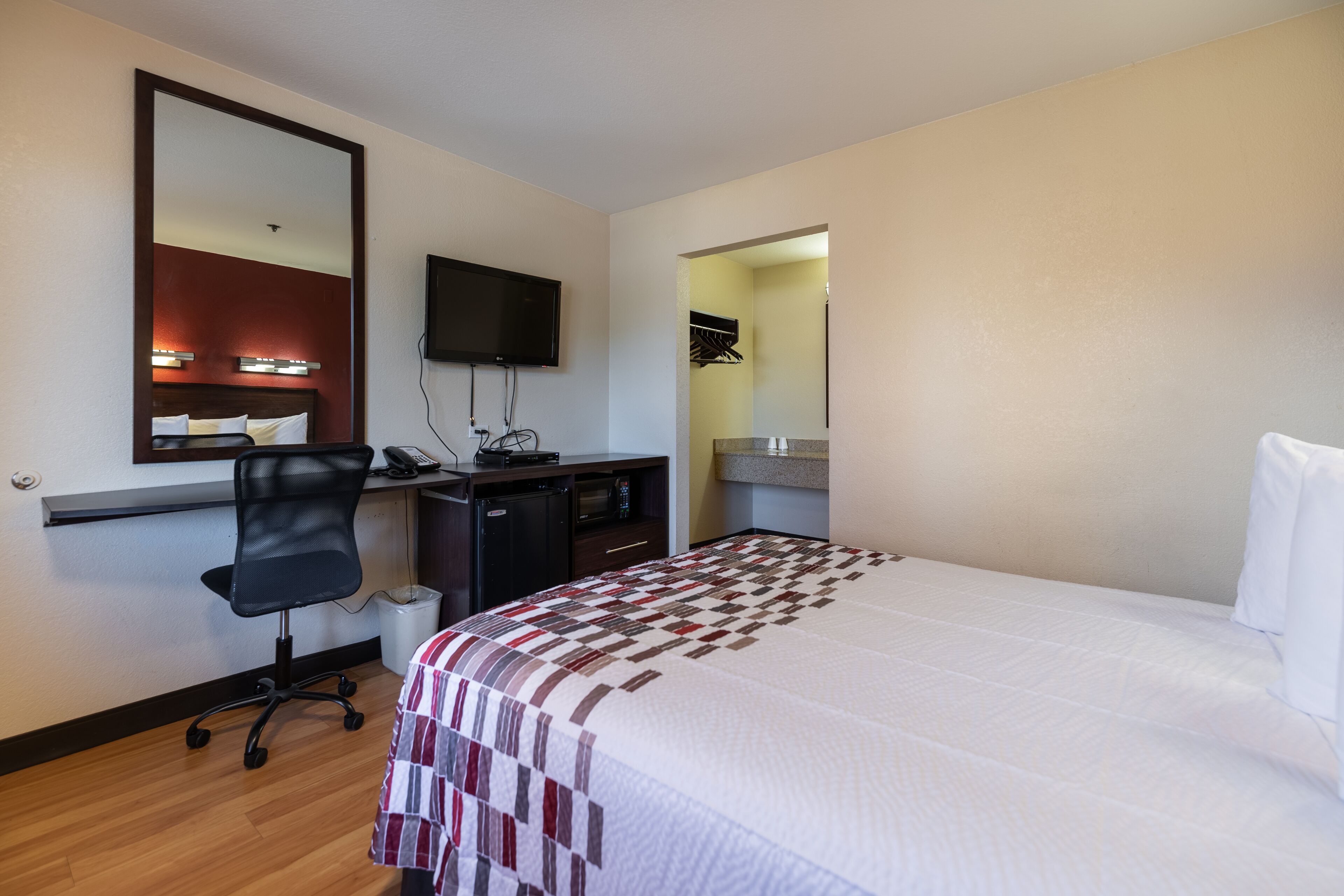 A hotel room with a bed, a desk with a computer, a chair, a TV, and a mirror.