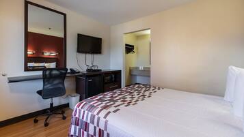 A hotel room with a bed, a desk with a computer, a chair, a TV, and a mirror.
