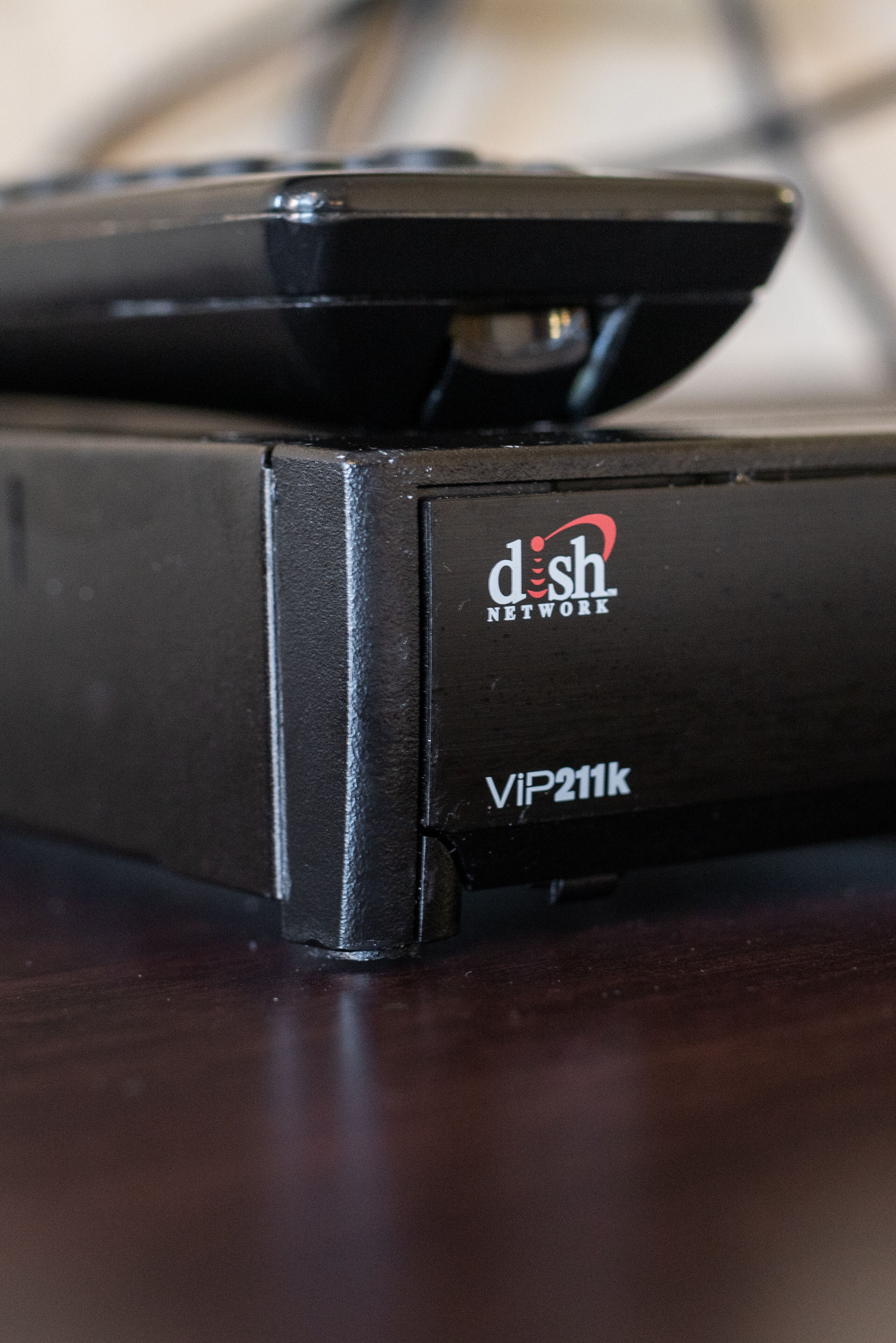 A black device with the label "dish network VIP211k" on a wooden surface.