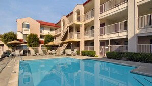 A hotel with a swimming pool, outdoor seating, and a multi-story building with balconies. - California Inn & Suites Rancho Cordova - Sacramento (Rancho Cordova)