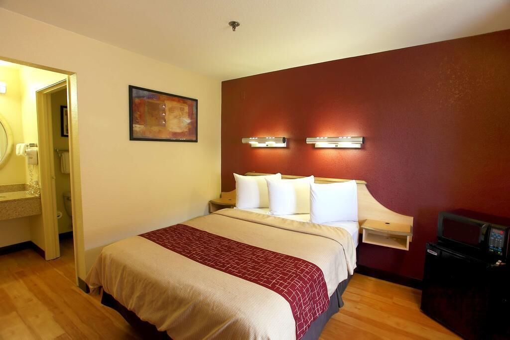 Habitació d'hotel amb un llit, una taula de nit, una làmpada penjada a la paret, un quadre i un microones.
