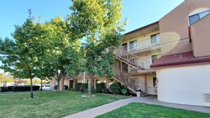 A multi-story building with a central staircase, a grassy courtyard, and a parking lot in the background. - California Inn & Suites Rancho Cordova - Sacramento (Rancho Cordova)
