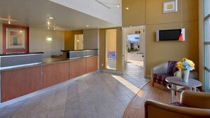 A reception area with a counter, a TV mounted on the wall, and a seating area with a table and chairs. - California Inn & Suites Rancho Cordova - Sacramento (Rancho Cordova)
