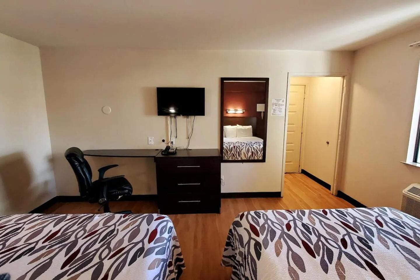A hotel room with two beds, a desk with a computer, a chair, and a TV.