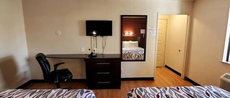A hotel room with two beds, a desk with a computer, a chair, and a TV.
