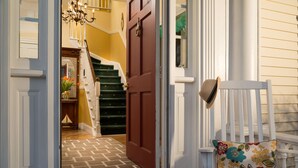 A staircase leading to a room with a patterned rug, a red door, and a white bench with a floral cushion. - Beech Tree Inn & Cottage (Newport)