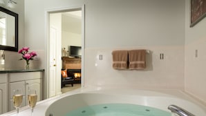 A bathroom with a large bathtub, two glasses of champagne, and a vase of pink flowers. - Beech Tree Inn & Cottage (Newport)