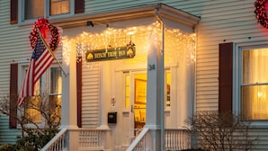 A front porch of a BEECH TREE INN with a sign, American flag, and Christmas lights. - Beech Tree Inn & Cottage (Newport)