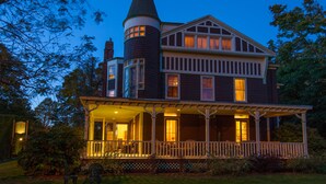 A large, two-story house with a prominent tower, a wrap-around porch, and a well-maintained garden. - Ivy Lodge Bed & Breakfast (Newport)