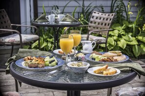 A round table with breakfast items including toast, fruit, and juice, set on a patio with chairs and plants in the background.