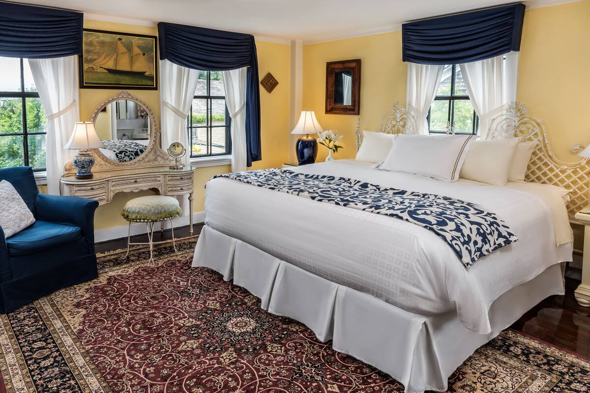 Una camera d'albergo con un letto grande, una toeletta con specchio, una poltrona blu e un tappeto decorato.