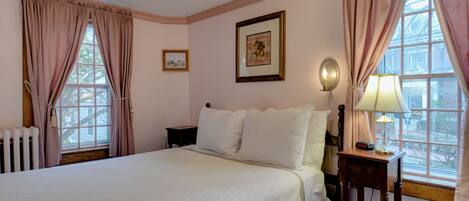 Une chambre à coucher avec un grand lit, une table de chevet avec une lampe, un tableau encadré au mur et une fenêtre avec des rideaux.