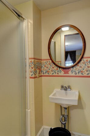 A bathroom with a white sink, a mirror, and a shower door. - Melville House (Newport)