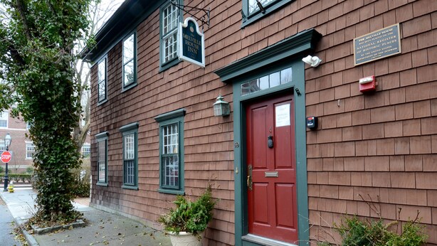 A historic building with a red door, a sign indicating it is a National Register of Historic Places, and a small planter with plants in front. - Melville House (Newport)