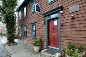 A historic building with a red door, a sign indicating it is a National Register of Historic Places, and a small planter with plants in front. - Melville House (Newport)