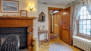 A cozy room with a fireplace, wooden furniture, and a view through a window with curtains. - Melville House (Newport)