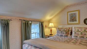 A bedroom with a bed, a nightstand, a lamp, a window with curtains, and a floral-patterned wall.