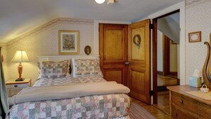 A bedroom with a bed, a nightstand, a dresser, a wooden door, and a wall with a framed picture. - Melville House (Newport)