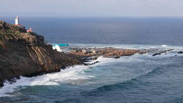 Un edificio costero con un faro, acantilados rocosos y olas rompiendo en la orilla.