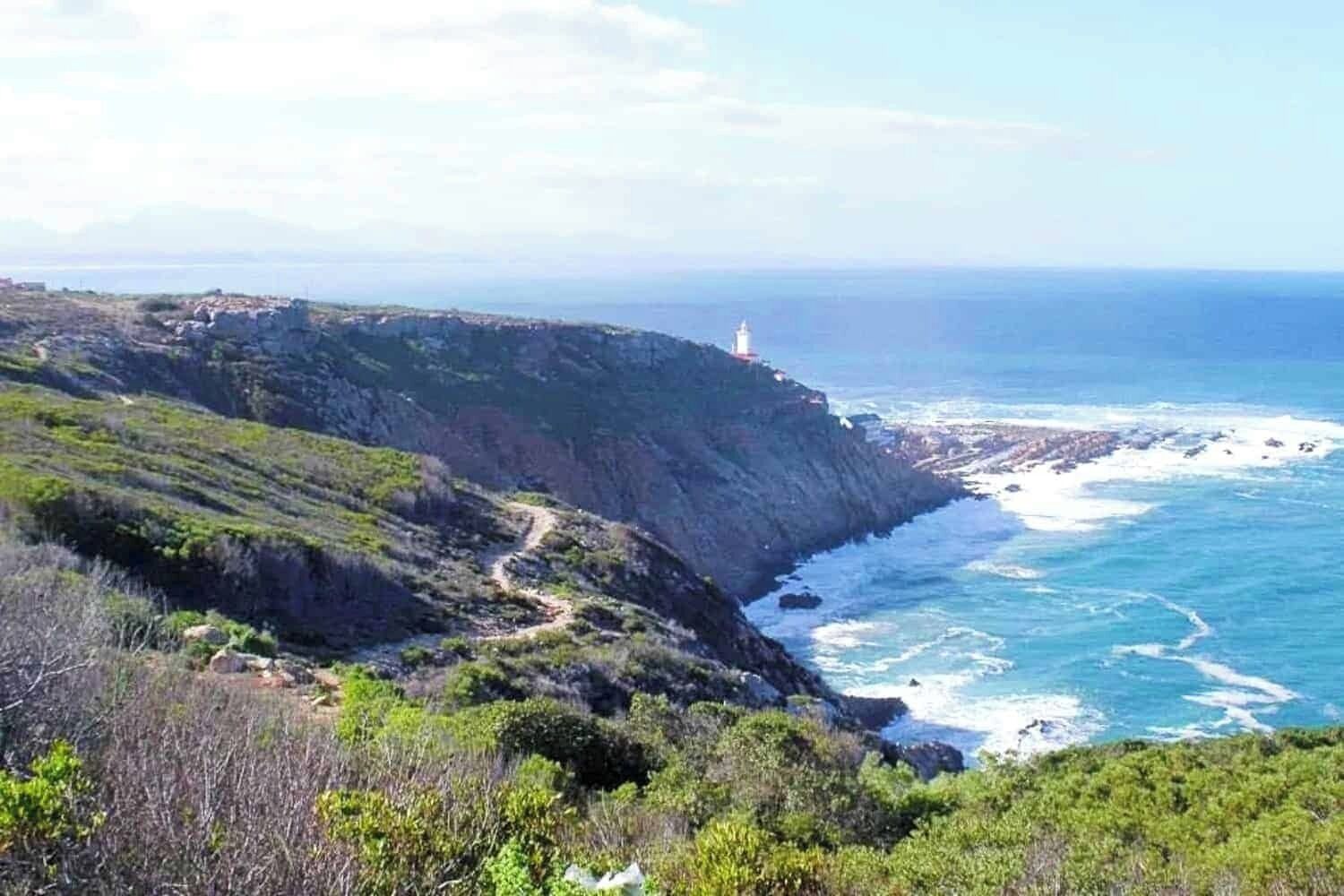A coastal landscape with a lighthouse on a cliff, a rocky shoreline, and a clear view of the ocean.