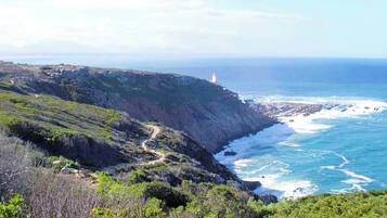 A coastal landscape with a lighthouse on a cliff, a rocky shoreline, and a clear view of the ocean.